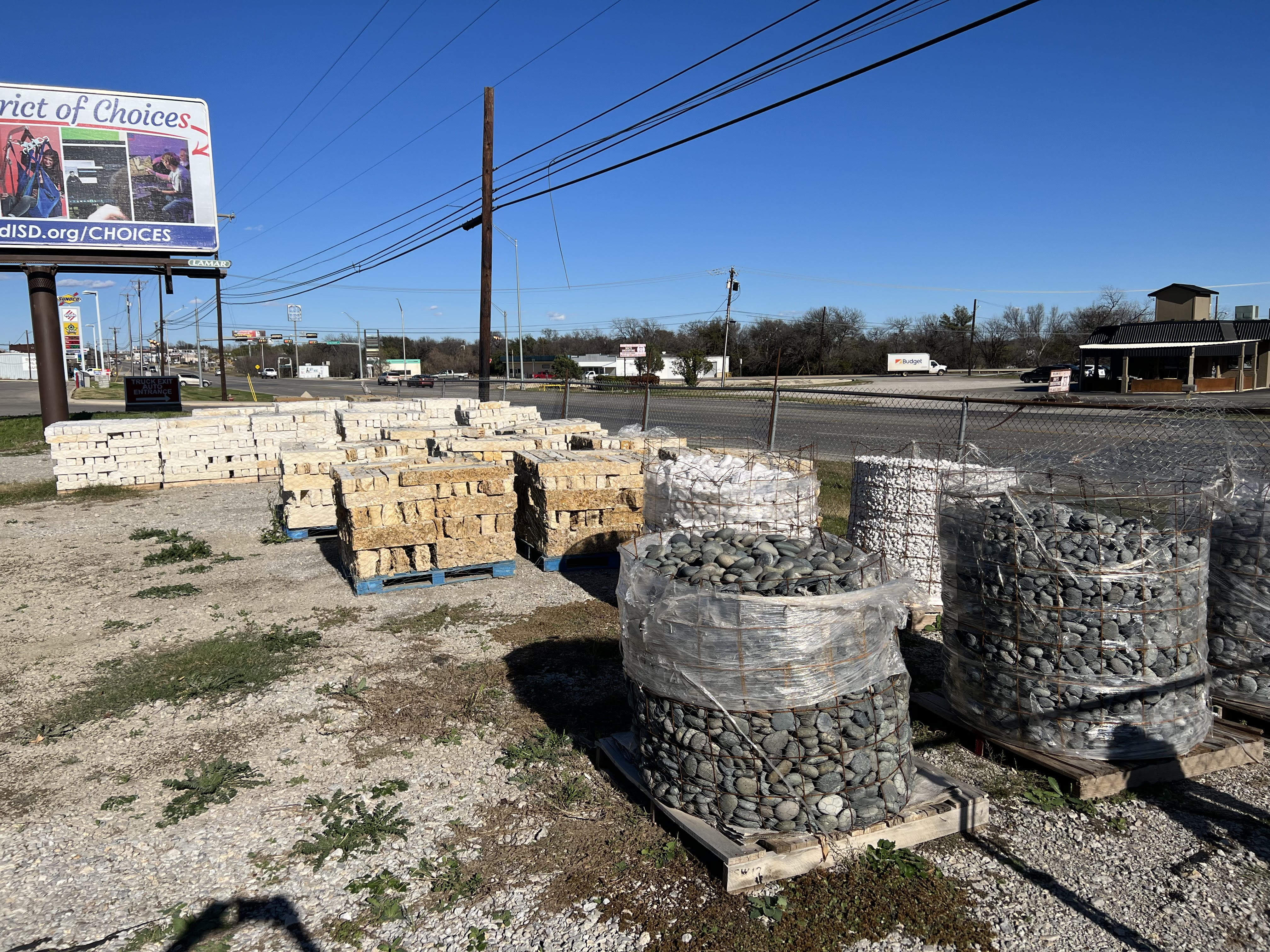 Wire baskets of river rock and white pea gravel staged for landscaping in the Brownwood, TX supply yard