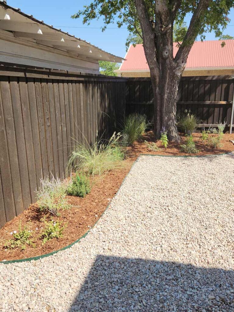 Decomposed granite roadbase path and graded fill dirt landscaping along a backyard flower bed, an example of topsoil, fill dirt, and road base work by Trees Forever Nursery in Brownwood, TX